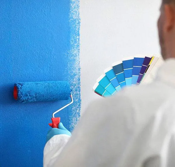 Pintor aplicando pintura azul con rodillo mientras sostiene una carta de colores