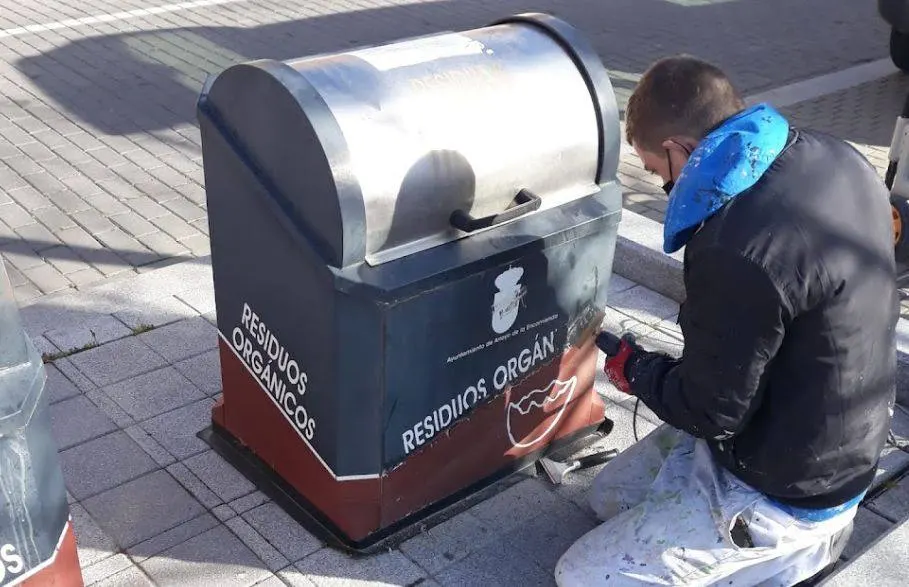 Pintor restaurando la pintura de un contenedor de residuos orgánicos en la calle