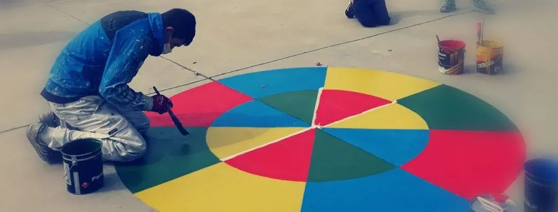 Pintor del equipo pintando un círculo de colores en el suelo de un patio